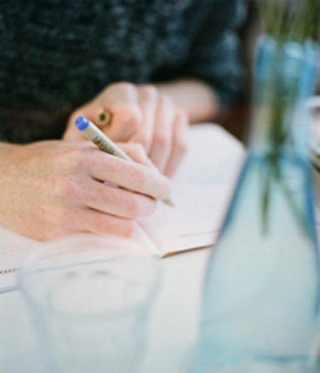 A person writing in a notebook with a blue felt-tipped pen.